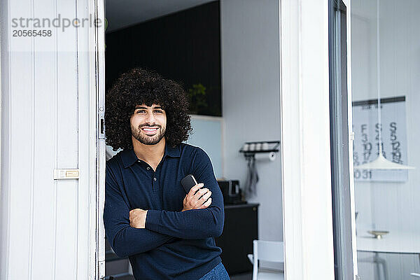 Smiling businessman with arms crossed leaning on doorway