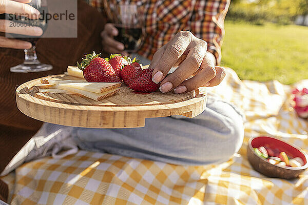 Hand of woman picking strawberry from cheese board