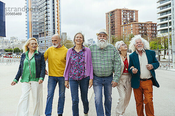 Carefree elderly friends walking together on street in city