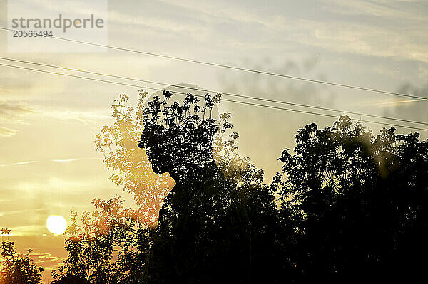 Multiple exposure of man with trees and sky at sunset