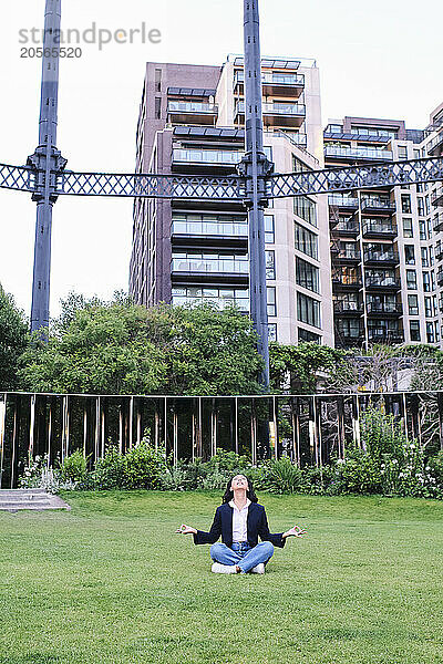 Businesswoman doing yoga sitting on grass at office park