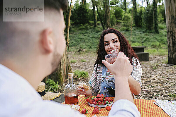 Happy woman toasting drinks with boyfriend in forest