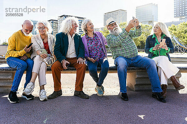 Man with smart phone taking selfie by friends sitting together on bench