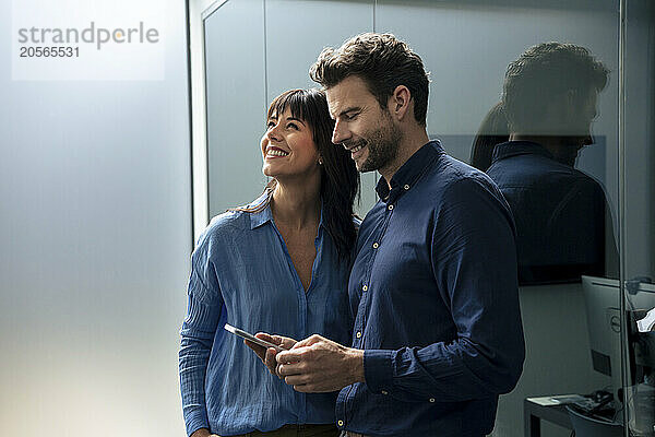 Happy businesswoman standing with businessman holding mobile phone in home office