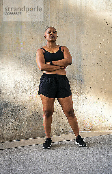 Confident sporty woman with arms crossed standing in front of wall