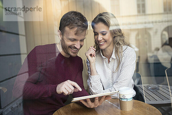 Happy couple using tablet PC and sitting in cafe