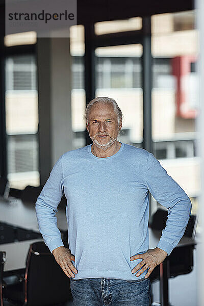 Confident businessman with arms akimbo standing in board room at office