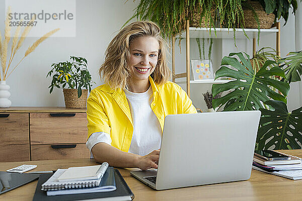 Smiling freelancer working on laptop sitting at desk in home office