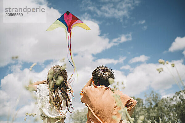 Girl flying kite by brother on sunny day