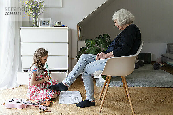 Girl playing flute sitting by grandmother at home