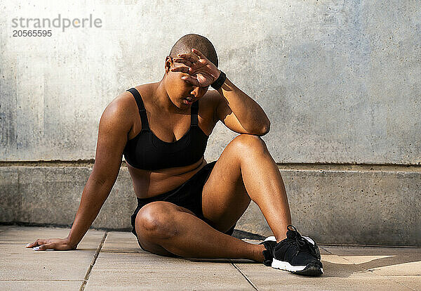 Tired woman sitting after workout near wall