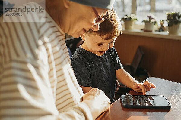 Boy and grandmother enjoying game on smart phone at home