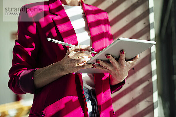 Businesswoman with tablet PC and digitized pen standing under sunlight at office