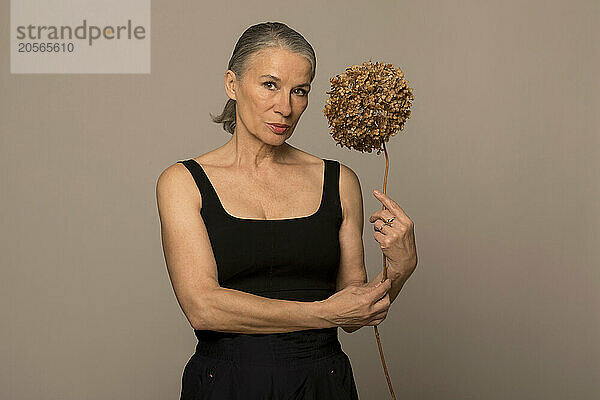 Confident woman holding withered flower against brown background