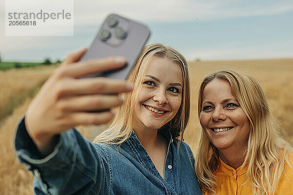 Happy daughter taking selfie with mother through smart phone at wheat field