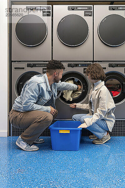 Couple removing sheet from washing machine squatting in laundromat