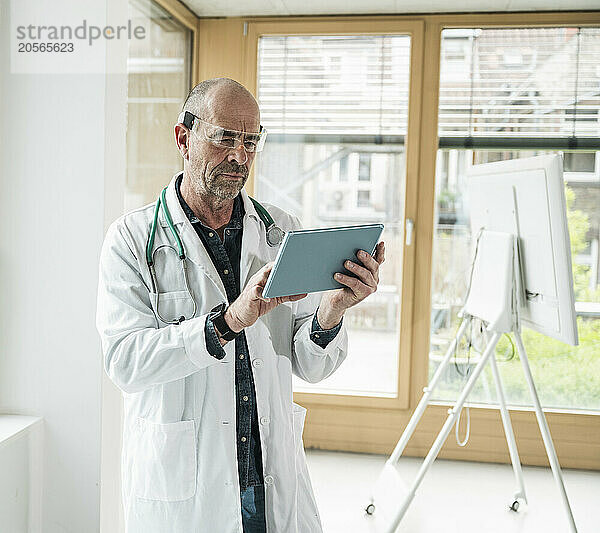 Confident mature doctor wearing smart glasses using tablet PC at hospital