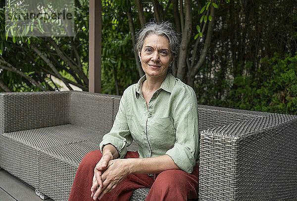 Smiling gray hair woman sitting on sofa at terrace