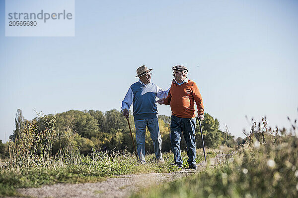 Senior man discussing and walking with friend at field