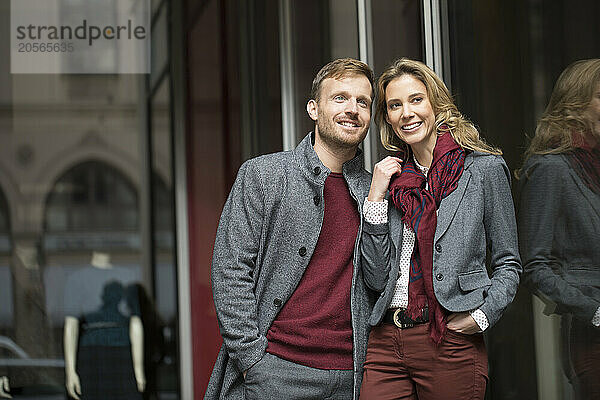 Happy girlfriend standing with boyfriend near glass wall