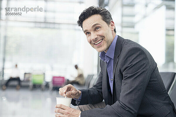 Happy businessman sitting with disposable coffee cup at airport