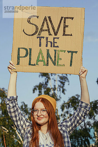 Smiling redhead girl in knit hat holding banner for protest