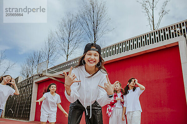 Happy teenage girl gesturing horn sign with friends at playground