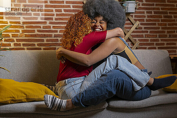 Happy young woman embracing roommate sitting on sofa at home