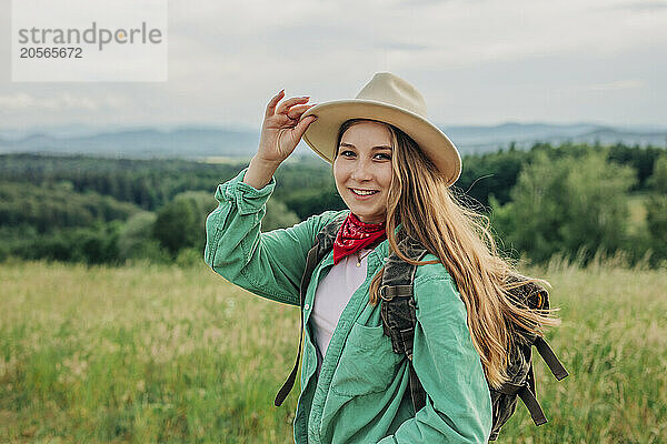 Beautiful young woman holding hat and hiking on mountain