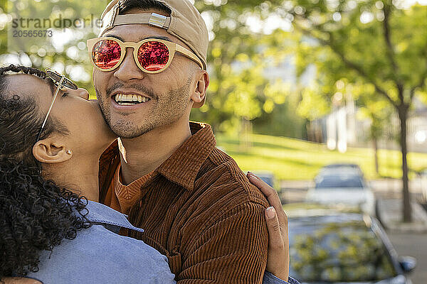 Young woman kissing boyfriend wearing sunglasses at park