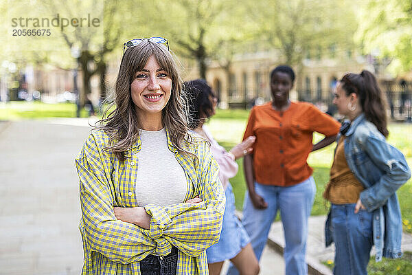 Smiling young woman with arms crossed standing in front of friends