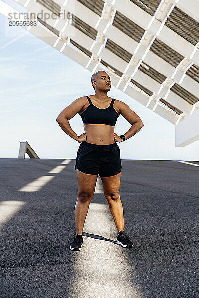 Confident sporty woman with arms akimbo standing on road