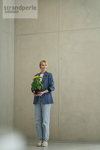 Businesswoman standing with sunflower plant in office lobby