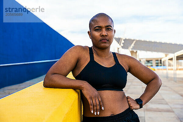 Bald woman standing with hand on hip near wall