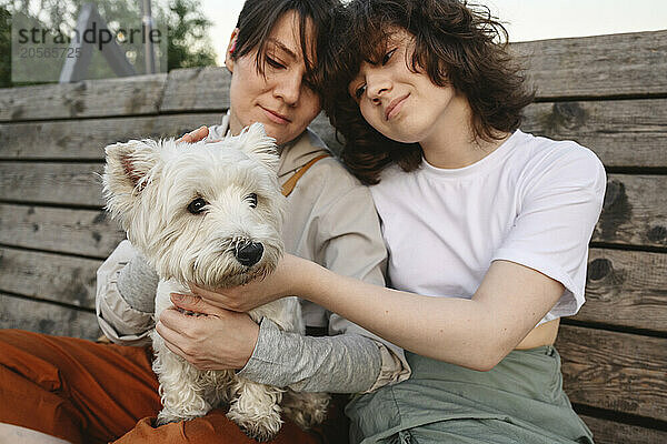 Mother and daughter sitting with white dog at park