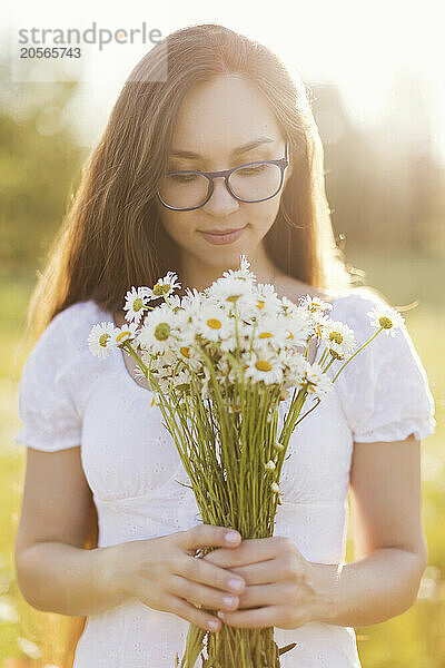 Young woman holding bunch of fresh chamomile in field