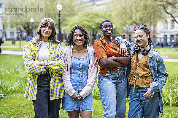 Smiling female friends standing side by side at park