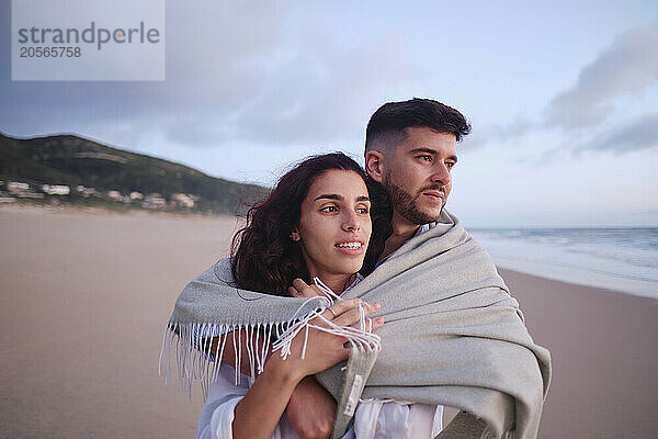 Young couple covered in blanket at beach