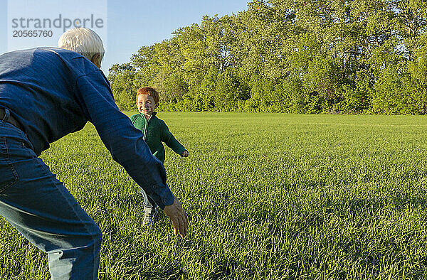 Smiling boy running towards grandfather standing on grass