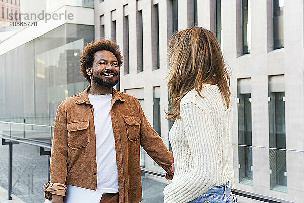 Smiling multiracial couple talking in front of modern building