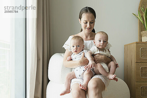 Happy mother holding sons and sitting on chair at home