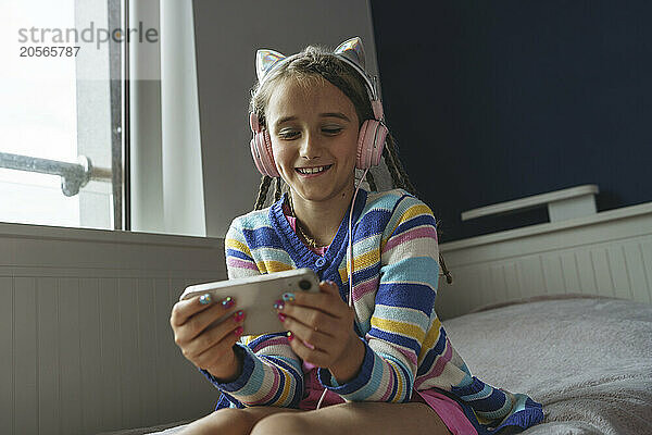 Happy girl listening wearing headphones watching movie on mobile phone at home