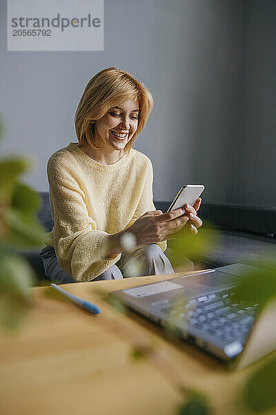 Smiling freelancer using smart phone at home office