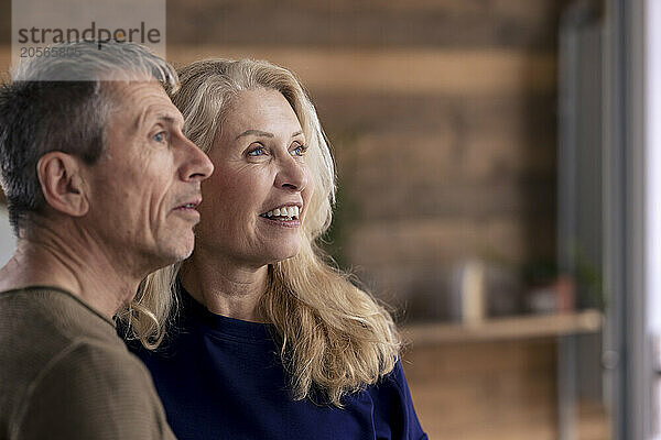 Smiling blond senior woman with man looking away at home