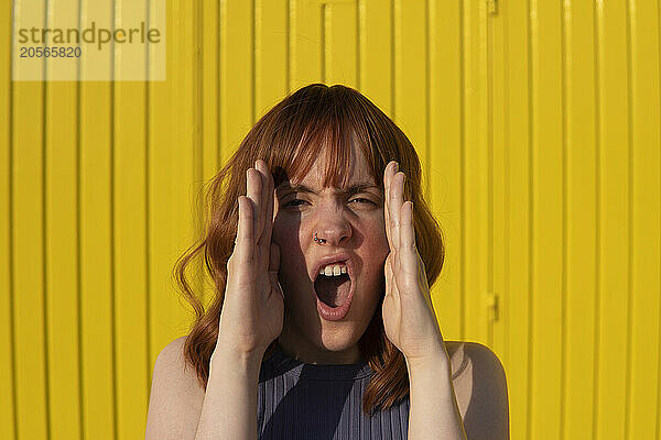 Redhead woman with mouth open in front of yellow wall on sunny day