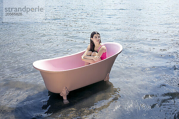 Girl sitting inside pink bathtub in lake on sunny day