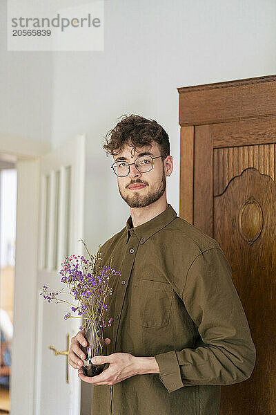 Confident young handsome man with flowers in vase at home