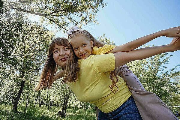 Happy mother giving piggyback ride to daughter in garden