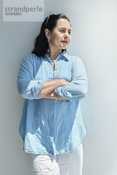 Businesswoman standing with arms crossed near wall