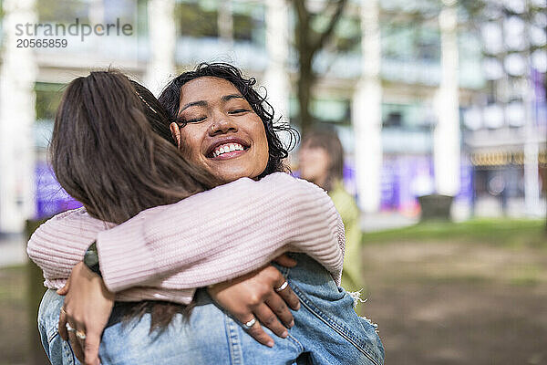 Smiling woman with eyes closed hugging friend at park